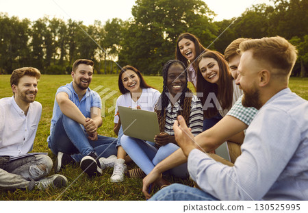 Happy diverse people sitting on grass in summer park, using laptop and having fun together 130525995