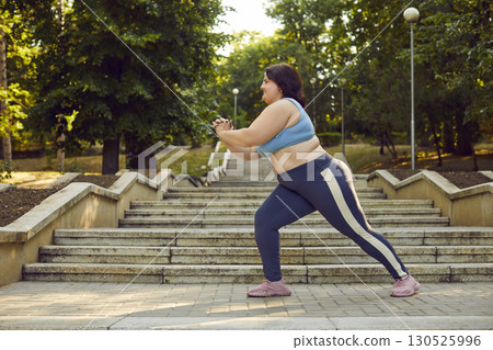Overweight fat woman in sportswear doing sport exercises in the summer city park. 130525996