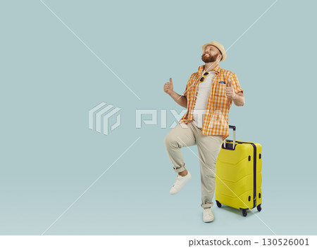 Funny young happy man in beach hat with yellow suitcase isolated on studio blue background. 130526001