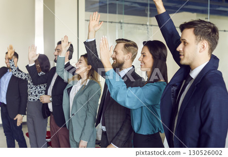Young cheerful company employees raising hands to vote at the conference standing in meeting room. 130526002
