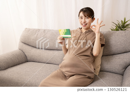 一名懷孕八個月的婦女坐在沙發上，手裡拿著一本存摺 130526121