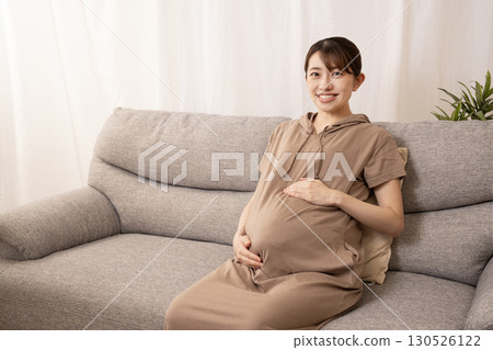 An eight-month pregnant woman sitting on a sofa and rubbing her stomach 130526122