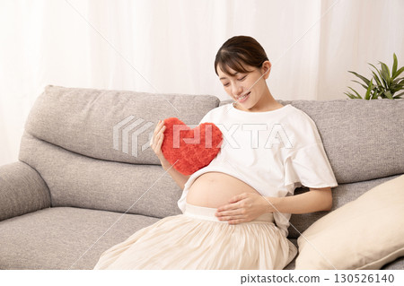 Eight-month pregnant woman sitting on a sofa and holding a red heart Eight-month pregnant woman sitting on a sofa and holding a red heart 130526140