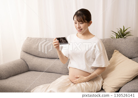 Pregnant woman sitting on sofa and holding ultrasound photo Pregnant woman sitting on sofa and holding ultrasound photo 130526141