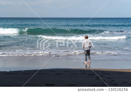 Boy stands barefoot on the wet sand of a northern beach looking at the waves Boy stands barefoot on the wet sand of a northern beach looking at the waves 130526256