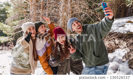 Friends taking selfie and gesturing peace sign in snowy forest 130526537