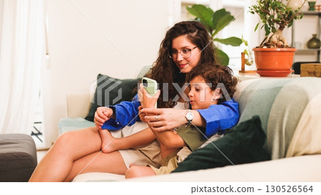 Mother and son watching smartphone sitting on sofa at home 130526564