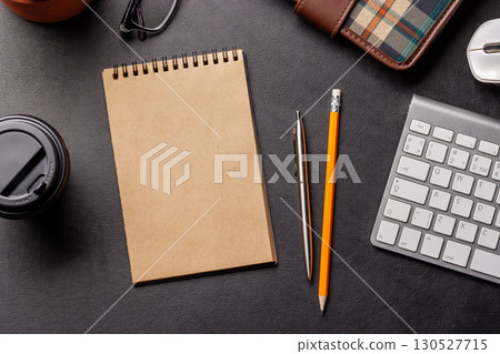 Top view of a dark leather office desk with notepad, supplies, and coffee cup 130527715