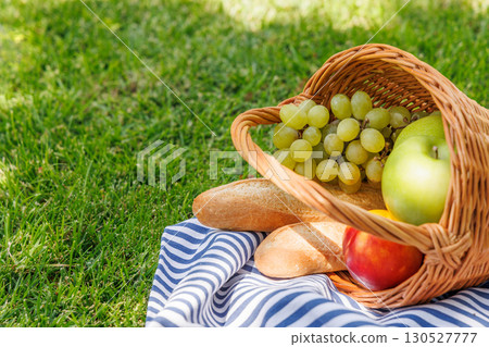 Picnic basket with fruits, and baguette on a sunny green meadow 130527777