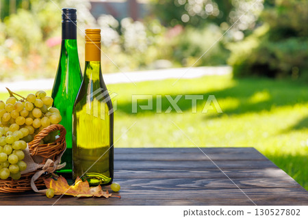 Wine bottles with grapes on a wooden table, glowing with sunny bokeh in the background Wine bottles with grapes on a wooden table, glowing with sunny bokeh in the background 130527802