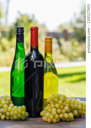 Wine bottles with grapes on a wooden table, glowing with sunny bokeh in the background Wine bottles with grapes on a wooden table, glowing with sunny bokeh in the background 130527803