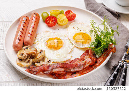 A classic breakfast plate featuring sunny-side-up eggs, crispy bacon, sausages, and fresh tomatoes 130527822