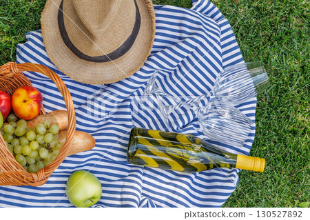 Picnic basket with wine, fruits, and baguette on a sunny green meadow Picnic basket with wine, fruits, and baguette on a sunny green meadow 130527892