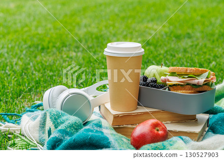 Minimal picnic setup on a lawn with books, sandwiches, fruits, and coffee 130527903