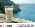A tall glass of milk is balanced on a ledge by the ocean. AI-generated content. 130528640