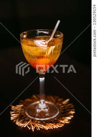 Sweet cocktail. Alcoholic mix drink. Yellow liquid served with orange lollipop in wineglass. Candy aroma beverage isolated on black. 130529154