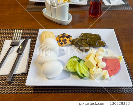 Breakfast plate with eggs, cheese, cucumber slices, grape leaves, and cookies served on a table. Nutrition, hospitality, and traditional cuisine in daily lifestyle. Breakfast plate with eggs, cheese, cucumber slices, grape leaves, and cookies served on a table. Nutrition, hospitality, and traditional cuisine in daily lifestyle. 130529253