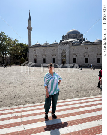 Woman standing in front of mosque courtyard with minaret in background. Culture, heritage, and travel representing architecture, tourism, and personal presence. 130529352