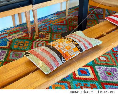 Ethnic patterned cushion on wooden bench with colorful carpet in interior room. Traditional craft, cultural textile, and decorative lifestyle element representing comfort and heritage. Ethnic patterned cushion on wooden bench with colorful carpet in interior room. Traditional craft, cultural textile, and decorative lifestyle element representing comfort and heritage. 130529360