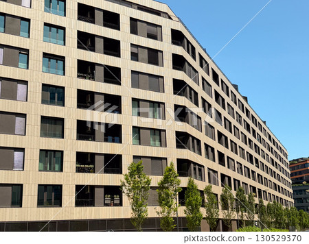 Close-up of modern apartment block facade with balconies and windows under blue sky. Contemporary architecture, housing development, and urban lifestyle symbolizing residential investment. 130529370