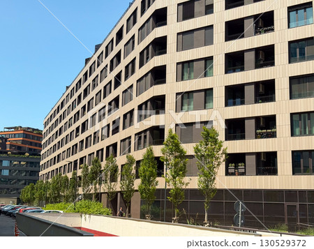Close-up of modern apartment block facade with balconies and windows under blue sky. Contemporary architecture, housing development, and urban lifestyle symbolizing residential investment. 130529372