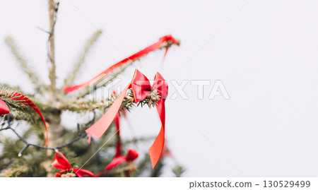 Red small bows is hanging from a Christmas tree outdoors on white background. Holiday background 130529499