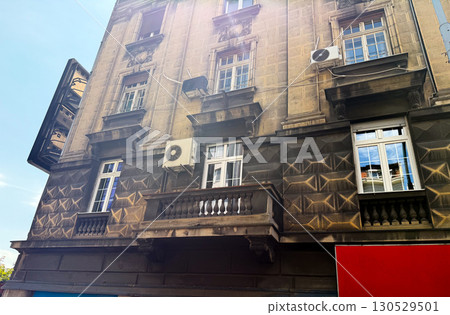 Old stone building with balconies, decorative reliefs, and textured facade in city. Architecture, heritage, and urban culture reflecting residential lifestyle, history, and neighborhood tradition. Old stone building with balconies, decorative reliefs, and textured facade in city. Architecture, heritage, and urban culture reflecting residential lifestyle, history, and neighborhood tradition. 130529501
