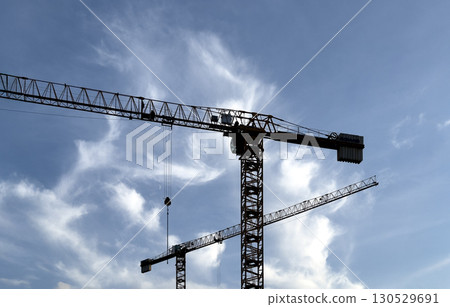 construction cranes stretch across a vivid sky with wispy white clouds, forming an intricate 130529691