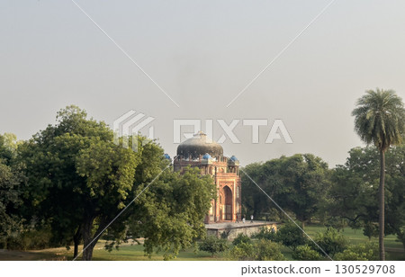 Distant view of Isa Khan s Tomb partially hidden by trees in a lush green landscape, with its dark Distant view of Isa Khan s Tomb partially hidden by trees in a lush green landscape, with its dark 130529708