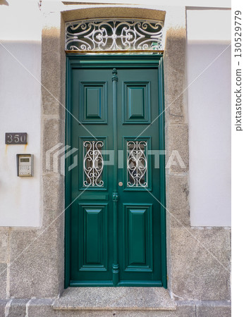 Elegant green wooden door with decorative white iron grilles and ornate transom, set in a stone Elegant green wooden door with decorative white iron grilles and ornate transom, set in a stone 130529779