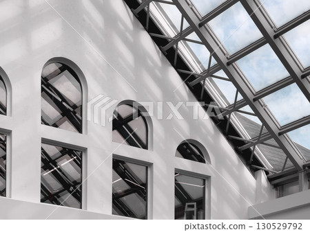 Interior view of a modern building with arched windows and a glass roof structure. Natural light 130529792