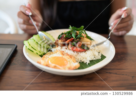 Close-up of woman in restaurant eating Thai holy basil seafood dish with fried egg and rice 130529986