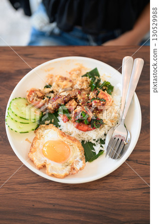 Close-up of woman in restaurant eating Thai holy basil seafood dish with fried egg and rice Close-up of woman in restaurant eating Thai holy basil seafood dish with fried egg and rice 130529988