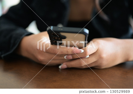 Close-up of woman hands texting and chatting using mobile phone indoors in coffee shop restaurant 130529989