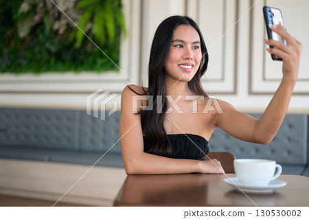 Beautiful young woman sitting in cafe using mobile phone while having coffee cup on table Beautiful young woman sitting in cafe using mobile phone while having coffee cup on table 130530002