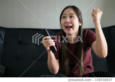Thai woman sitting on sofa watching television at home looking happy and excited Thai woman sitting on sofa watching television at home looking happy and excited 130530037