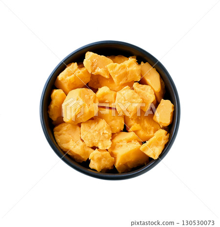 pieces of matured cheddar in black ceramic bowl isolated on white background. Top iew. 130530073