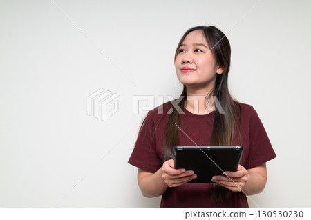 Studio portrait of young Asian woman using digital tablet computer while thinking and looking up Studio portrait of young Asian woman using digital tablet computer while thinking and looking up 130530230