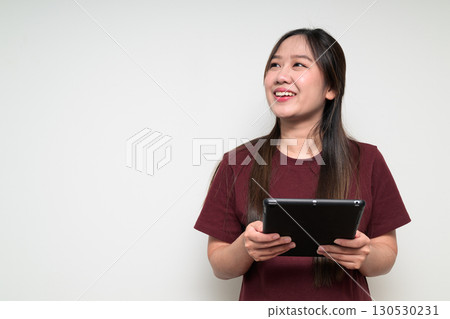 Studio portrait of young Asian woman using digital tablet computer while thinking and smiling 130530231