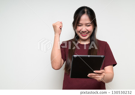 Studio portrait of young Asian woman using digital tablet computer looking excited with arm raised Studio portrait of young Asian woman using digital tablet computer looking excited with arm raised 130530232