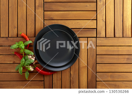 Empty black plate, garlic, basil, and red pepper on a natural wooden background. Empty black plate, garlic, basil, and red pepper on a natural wooden background. 130530266