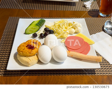 Breakfast plate with boiled eggs, cheese, sausage, vegetables, and pastry. Nutrition, food culture, and lifestyle in hotel dining service. Breakfast plate with boiled eggs, cheese, sausage, vegetables, and pastry. Nutrition, food culture, and lifestyle in hotel dining service. 130530673