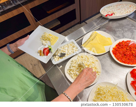 Person selecting cheese and vegetables at buffet with plate in hand. Lifestyle, hospitality, and nutrition in hotel breakfast environment. Person selecting cheese and vegetables at buffet with plate in hand. Lifestyle, hospitality, and nutrition in hotel breakfast environment. 130530678