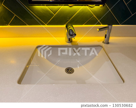 Modern bathroom sink with chrome faucet and yellow light reflection. Hygiene, interior design, and lifestyle details in daily environment. Modern bathroom sink with chrome faucet and yellow light reflection. Hygiene, interior design, and lifestyle details in daily environment. 130530682
