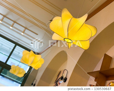 Yellow decorative ceiling lamp with modern floral shape in cafe interior. Lighting, design, and atmosphere in hospitality and contemporary lifestyle. 130530687