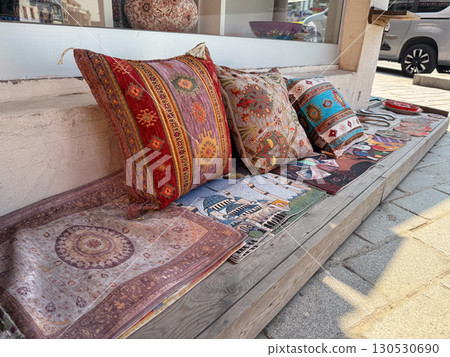 Assorted decorative pillows with traditional patterns arranged on outdoor bench. Textile craft, artisan heritage, and colorful display in cultural retail setting. Assorted decorative pillows with traditional patterns arranged on outdoor bench. Textile craft, artisan heritage, and colorful display in cultural retail setting. 130530690