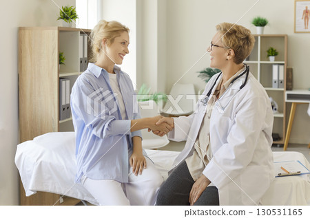 Female doctor and young patient shaking hands in clinic consultation room 130531165
