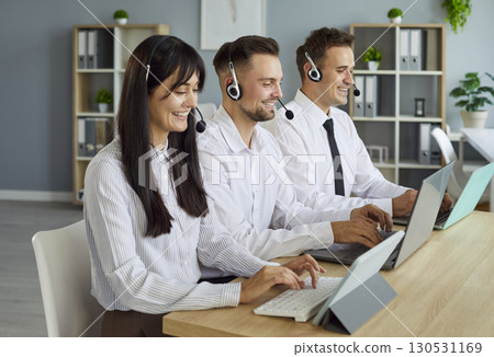 Smiling call center agents with headsets providing customer support at desks 130531169