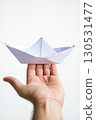 Close-up of hand holding white origami paper boat, simple craft symbolizing hope or childhood 130531477