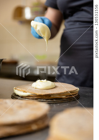 Pastry chef spreading cream on cake layer in professional bakery kitchen, close-up 130531556